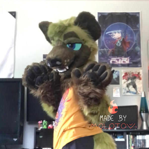 A person wearing the partial fursuit of Jin, a green hyena. Their paws are raised to shoulder level, and the front of their body is turned away from the camera.