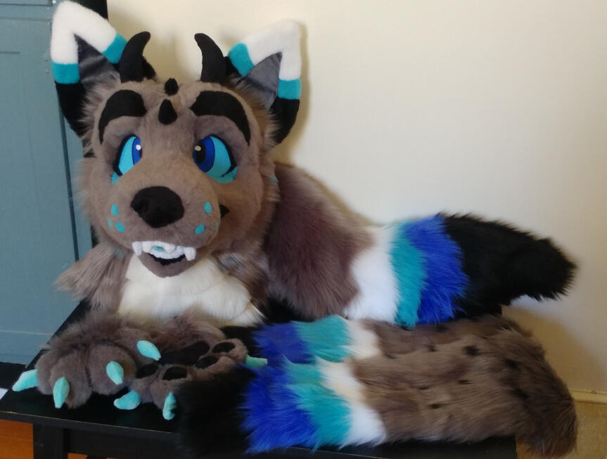 Another view of the head, paws, tail and arm sleeves of Zephyr, a grey and blue dragon wolf with black horns on his head.