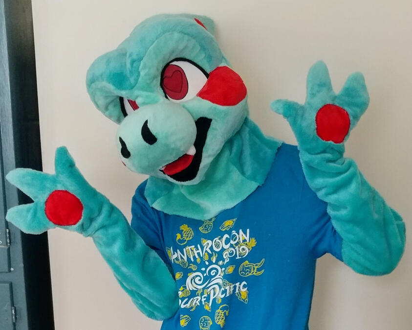 A person wearing the Clarence fursuit. They have their hands up and their head tilted to the side.